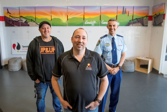 three men in front of a mural