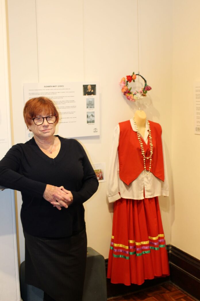 GretaMigrantCamp Maitland Regional Museum vice president Julie O’Donohue next to a Greta ethnic dance costume.