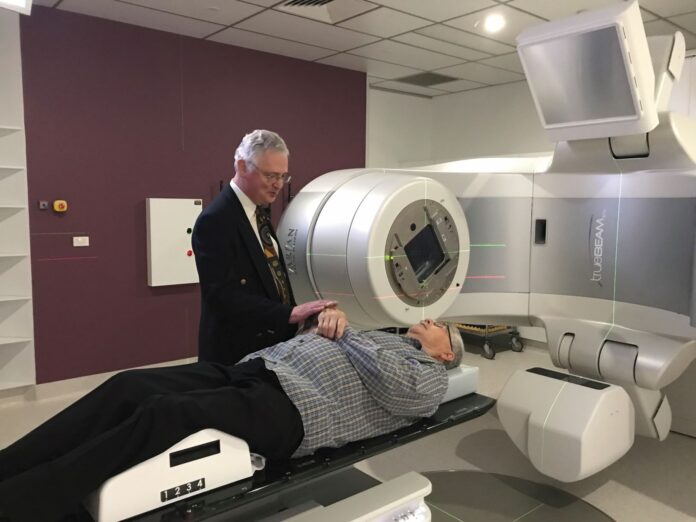 Professor Jim Denham in front of a Linear Accelerated, which delivers the radiation therapy