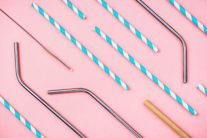 Flatlay of various eco sustainable straws for beverages: paper, metal and bamboo with special brush on pink