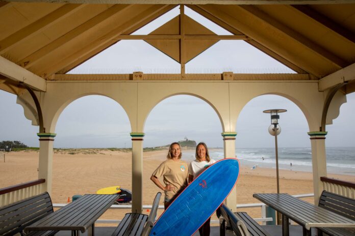 two women with a surfboard at the beach