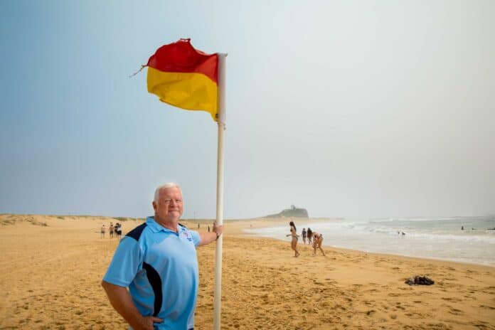 man next to red and yellow flag at beach
