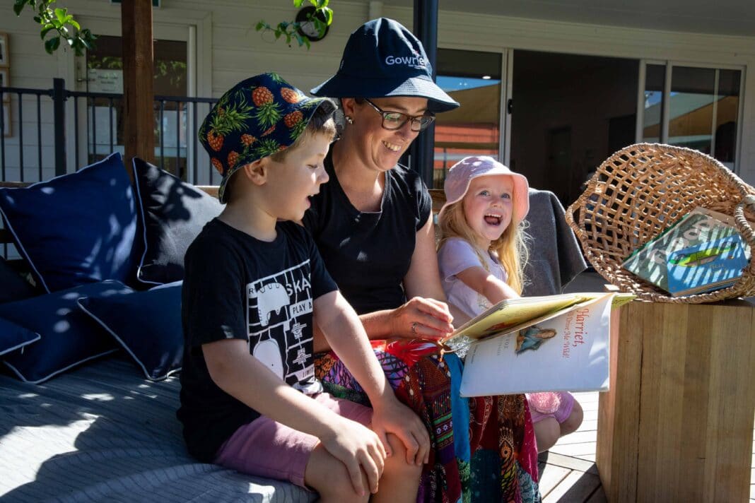 woman with two children reading a book outside