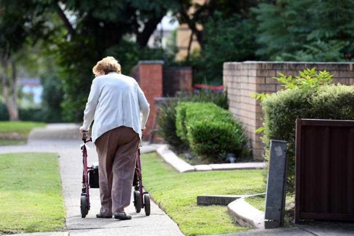 An elderly woman uses a mobility walker to walk down a suburban footpath
