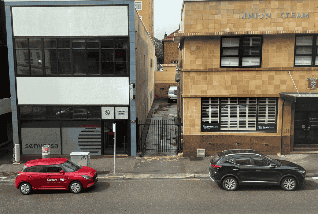 red suzuki swift parked infront of building in city with black car infront.